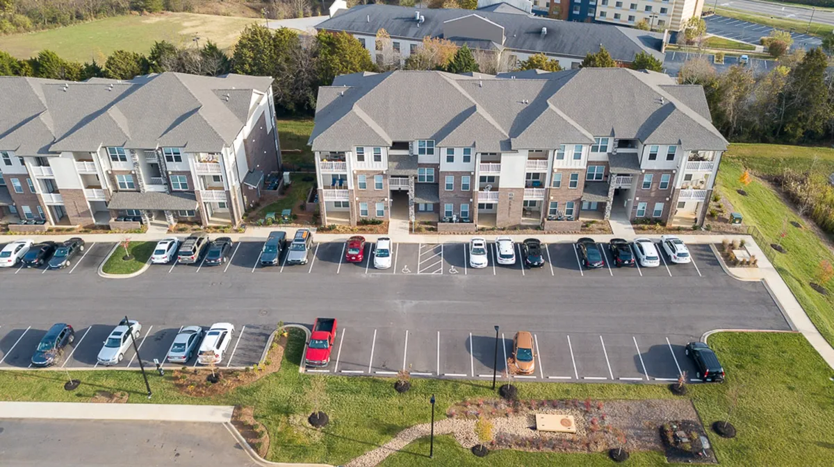 Wide-angle view of the apartment buildings set against a backdrop of green landscape and a welcoming parking area. The scene invites visitors to imagine beginning or ending their adventures with a peaceful stroll or morning coffee amidst the natural setting.