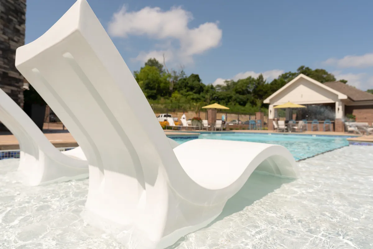 A serene swimming pool area with plush lounge chairs, a poolside cabana, and abundant surrounding greenery. The space is tranquil and perfect for both relaxation and socializing, with the sunset casting a serene glow over the water.