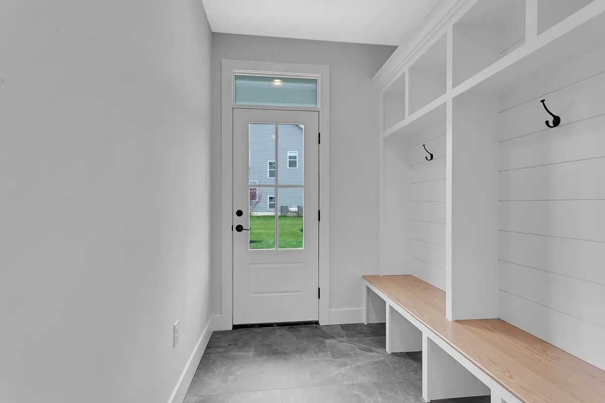 This image showcases the entryway with a sturdy door, a welcoming bench seat, and convenient coat hooks. The area is well-lit and thoughtfully designed for practical daily use, inviting residents and guests to transition comfortably from outside to inside.