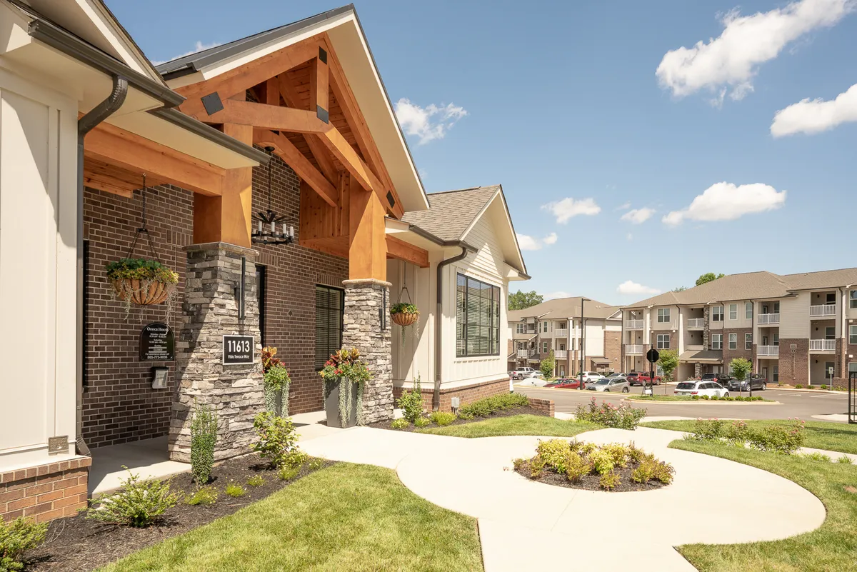 This image captures the entrance to the Overlook at Farragut community, featuring inviting wooden beams, stone accents, a landscaped pathway, and colorful flower planters. The attractive garden setting and welcoming architectural details immediately evoke a sense of arrival and exclusivity.
