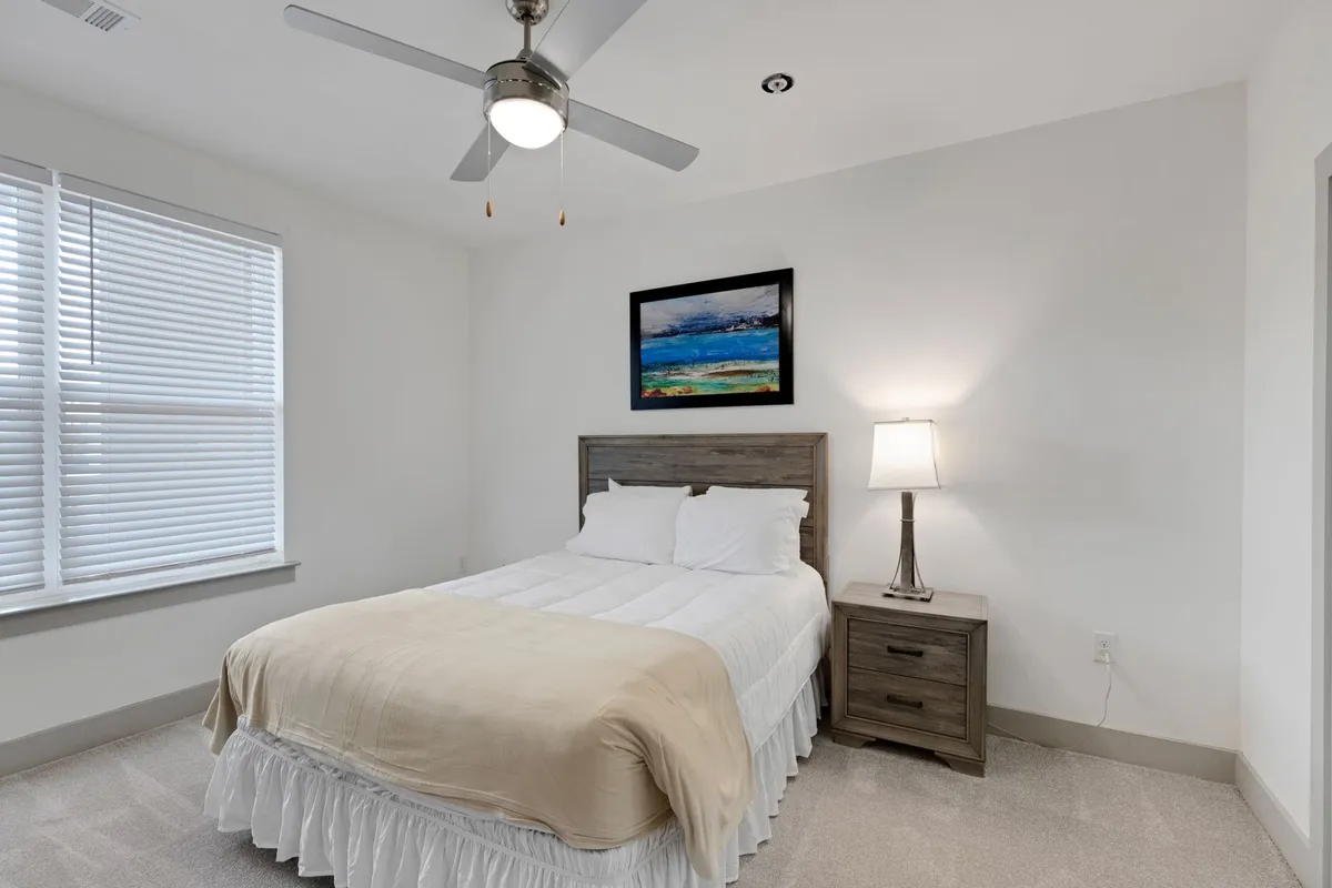 A peaceful bedroom scene with a cozy bed, nightstand, lamp, and wall artwork. The ambiance is quiet and inviting, with natural light filtering in, evoking a calming oasis for restorative sleep.