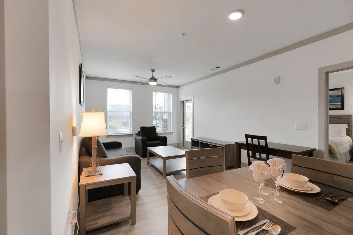 An inviting interior scene with a dining table set for a meal, comfortable seating nearby, and expansive windows that allow natural light to flood the space. The atmosphere is relaxed and welcoming, perfect for gathering or enjoying peaceful moments.