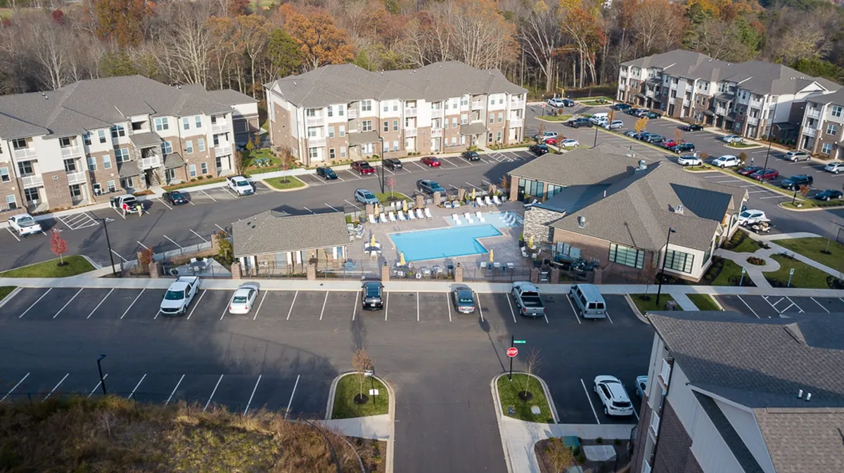 A wide view of the swimming pool framed by landscaped areas, with apartment buildings and a parking area visible in the background. The pool area is designed for relaxation and social gatherings, suggesting possibilities for family fun, sunbathing, and community events—perfect for unwinding after a day of adventures.