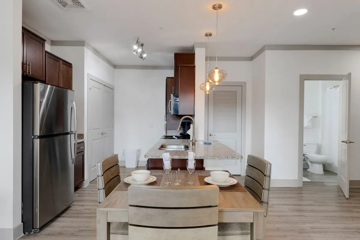 This image features a modern kitchen with a central island, a dining table set for meals, and sleek appliances. The space is inviting, with warm lighting enhancing the cozy yet stylish atmosphere. Both the kitchen and dining area are clearly visible, emphasizing the open layout and the seamless flow between cooking and dining.