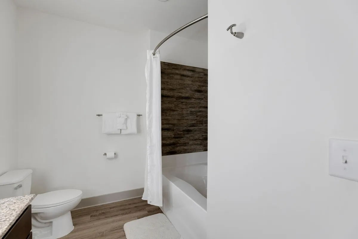 A fresh, inviting bathroom featuring a bathtub, toilet, sink, shower curtain, and neatly arranged towels. The space feels tranquil and rejuvenating, ideal for a soothing soak or quick refresh.