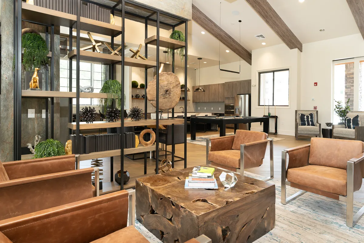 A cozy lounge area with leather chairs, a wooden coffee table, decorative shelving, and a view into an open kitchen. The space is intimate yet open, ideal for casual reading, pondering, or informal work sessions, with plenty of natural light contributing to a calm and welcoming atmosphere.