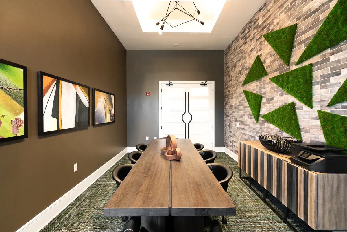 A stylish, modern interior featuring a long wooden table, black seating, bold geometric wall art, and a unique lighting fixture. The room is set up for collaborative meetings or quiet work, with ample light and a contemporary ambiance that promotes both focus and inspiration.